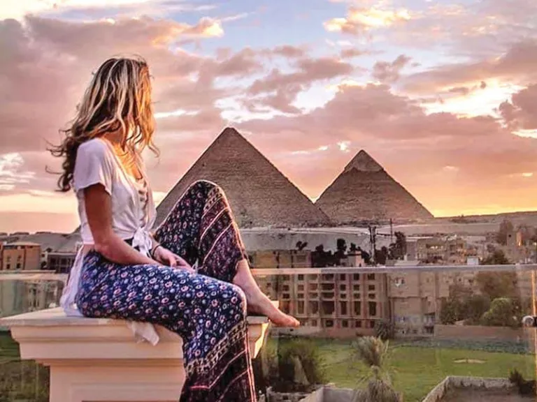 Woman sitting on a balcony watching the sunset over the Giza Pyramids—romantic Cairo travel experience.