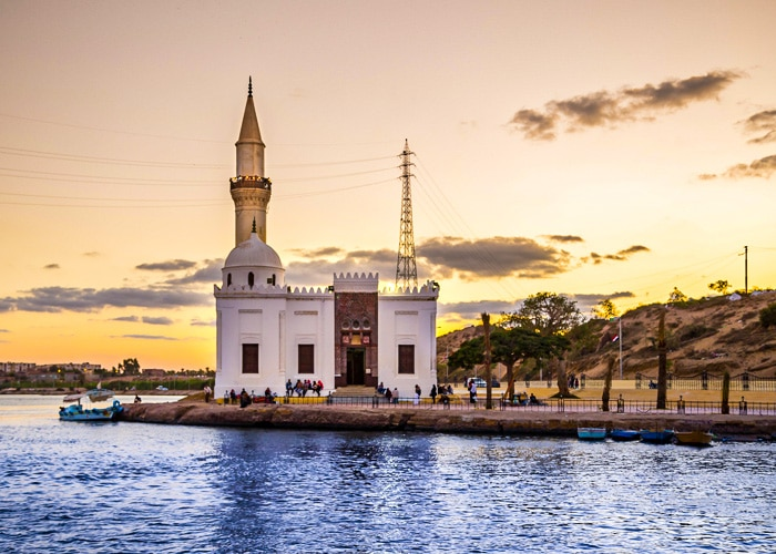 The picturesque Abou Mandour Mosque and lighthouse complex in Rosetta reflecting on the water during a scenic sunset.