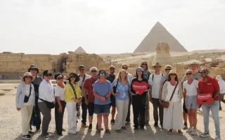 A happy group of international tourists with Ramses tour guides posing in front of the Great Sphinx and Giza Pyramids during a day trip from Alexandria.