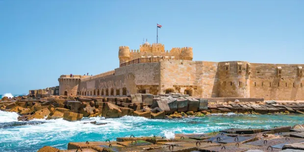 The Citadel of Qaitbay, a 15th-century defensive fortress on the Mediterranean coast in Alexandria, Egypt, under a clear blue sky.