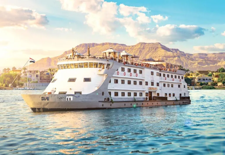 Luxury cruise on the Nile ship sailing past lush riverbanks and desert hills under a blue sky in Egypt.