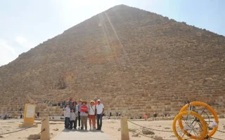 Tourists standing on a wooden walkway in front of the Great Pyramid of Khufu, with a guide holding a red heart sign during a Giza plateau tour.