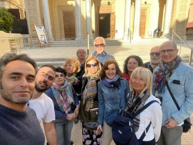 A tourist group posing for a photo in front of a grand historic building with classical columns in Egypt.