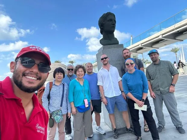 A group of tourists posing with a guide in front of the Alexander the Great statue at the Library of Alexandria.