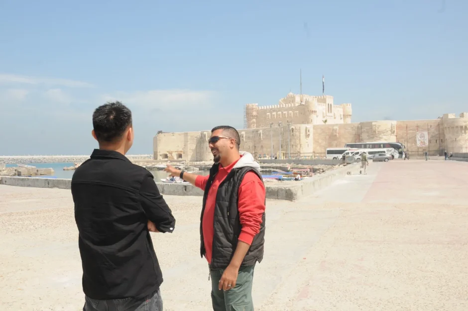 A professional guide sharing historical insights with a traveler on the waterfront near the Qaitbay Citadel.