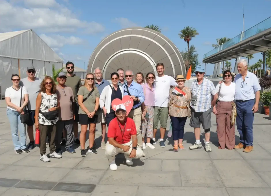 A large group of tourists posing with a Ramses Tours heart sign in front of the iconic tilted sun-disk architecture of the Library of Alexandria, Egypt.