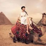 A woman in a white dress riding a camel in front of the Giza Pyramids, a classic activity of tourism in Egypt.