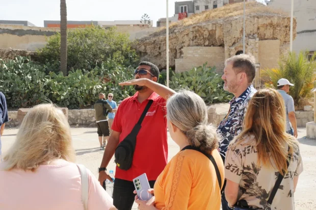 Tour guide leading a sightseeing group near ancient ruins and catacombs in Alexandria, Egypt.
