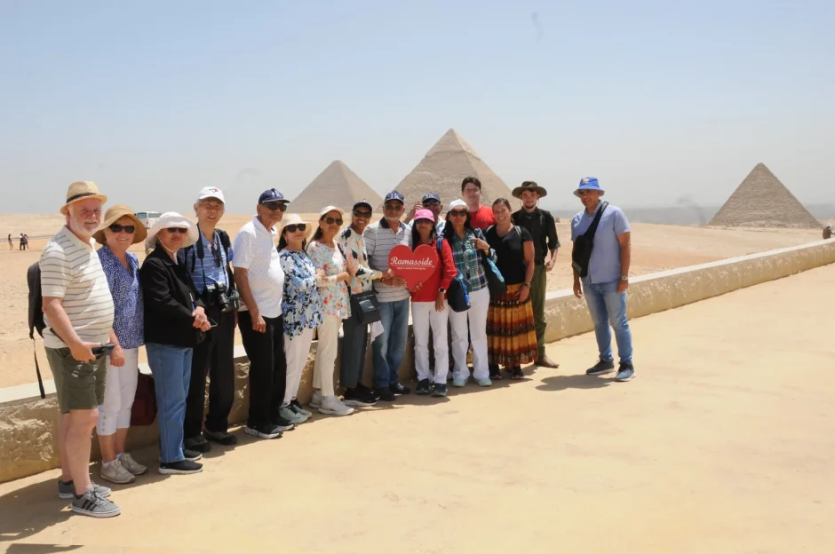 Tourists enjoy a visit to the Great Pyramid of Khufu in Giza with a panoramic view of the pyramids and a sunny desert backdrop.