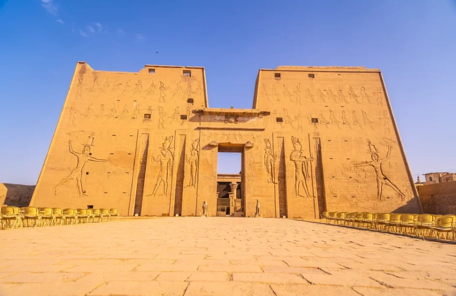 Front view of the Temple of Horus in Edfu featuring massive pylons with ancient Egyptian relief carvings and rows of chairs.