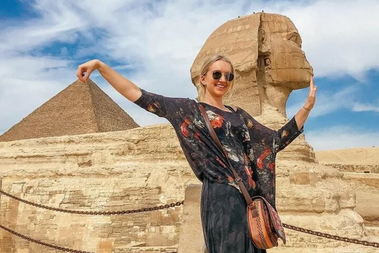 A happy tourist posing in front of the Great Sphinx and Pyramids of Giza during her sunny summer vacation in Egypt.